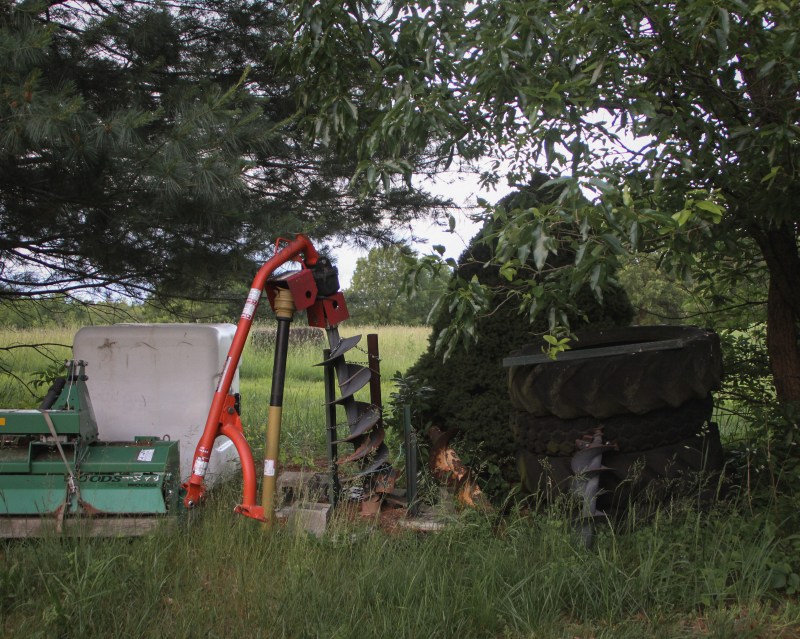 An outdoor picture taken of tools that are frozen in time. The grass grows high around the tools. 